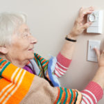 Senior woman saving energy by dressing warm and adjusting her thermostat.