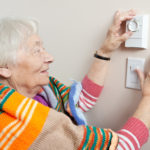 Senior woman saving energy by dressing warm and adjusting her thermostat.