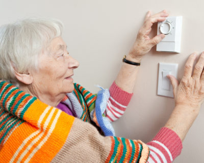 Senior woman saving energy by dressing warm and adjusting her thermostat.