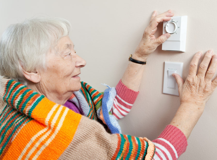 Senior woman saving energy by dressing warm and adjusting her thermostat.