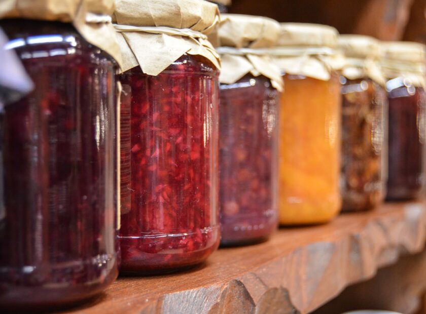 Jars of jam on a wooden shelf.